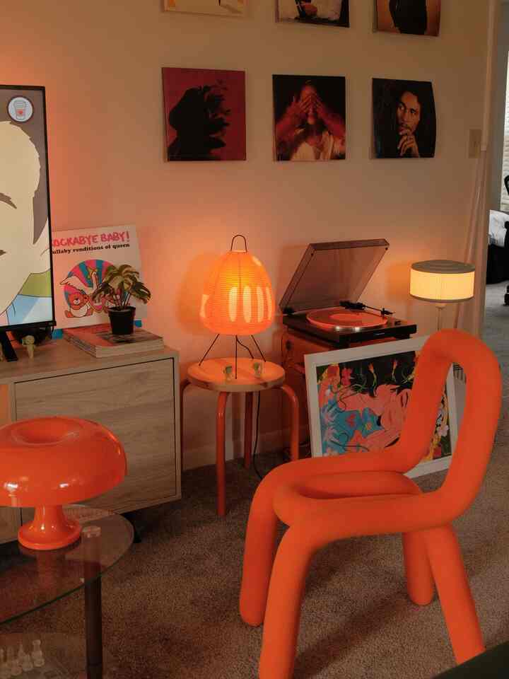 Orange-dominant living room featuring a funky boucle loop armchair, table lamp, retro turntable, and framed posters on walls creating a warm atmosphere