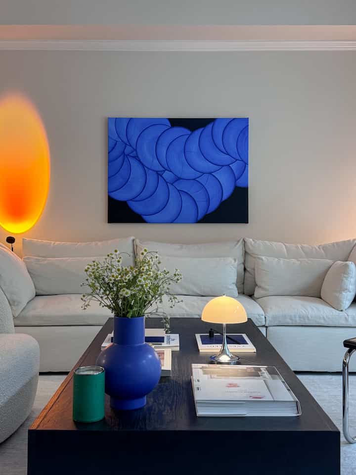 Modern living room with white sofa, blue wall art, and black coffee table arranged centrally