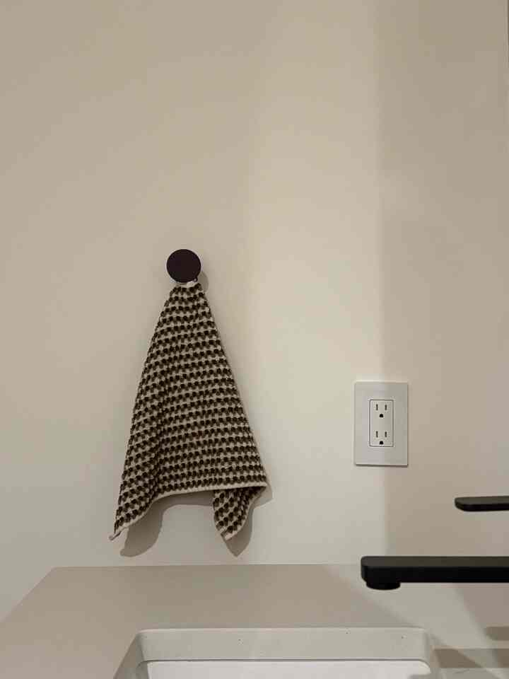 Clean bathroom wall in white and brown tones featuring a towel hanging on a wall hook and a power outlet