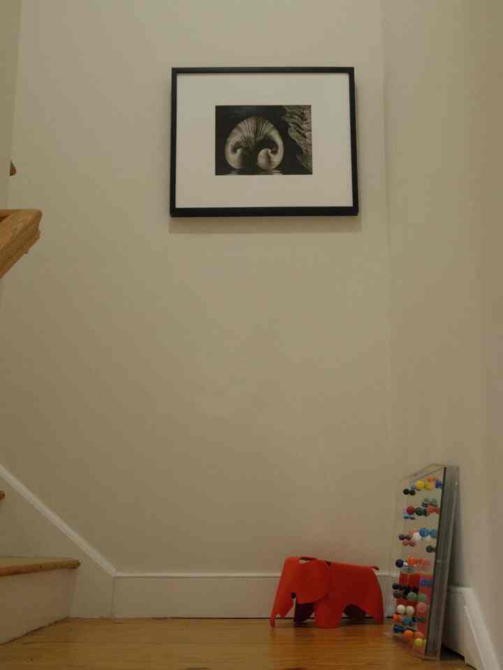 Beige walls and wood tone floor in a stair entrance area featuring an orange elephant objet and framed artwork with a simple atmosphere