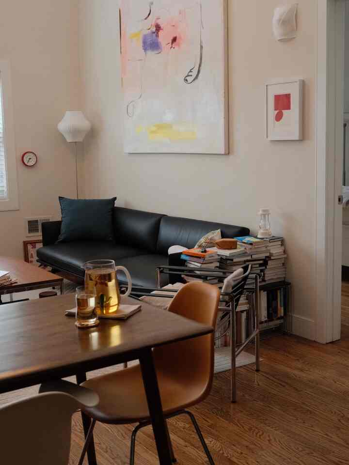 A simple living room with wood tone flooring, featuring a black sofa and mid-century modern furniture