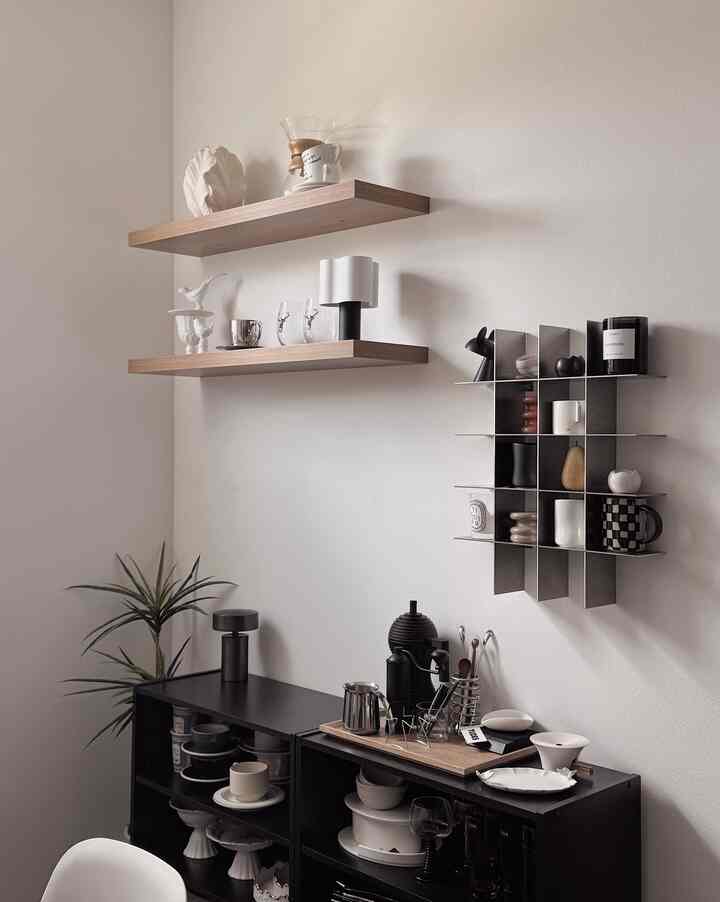 Natural color and black toned home cafe space featuring wall shelves and a black cabinet with coffee machine and various coffee tools in a modern interior