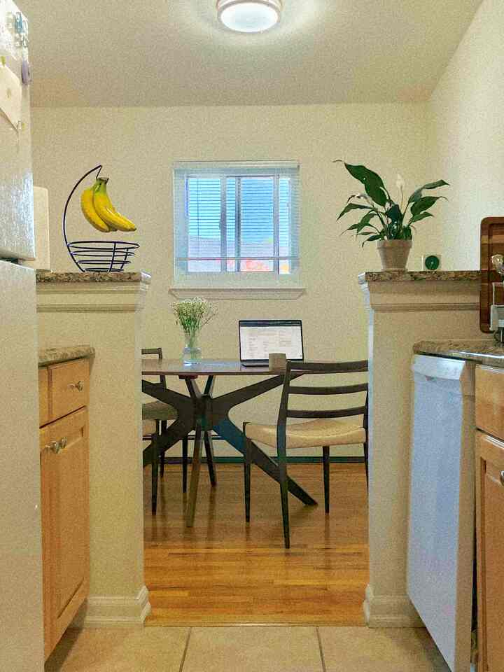 Bright kitchen and dining room with white walls and wood-tone flooring, featuring a dining table with laptop and transparent vase for a practical atmosphere