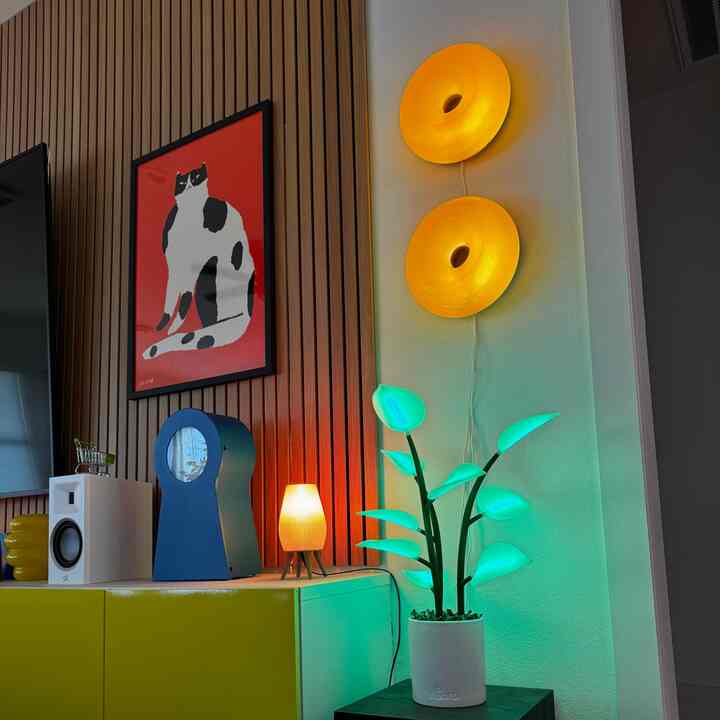 Natural-tone living room wall with a red cat poster, warm wall sconces, and green leaf-shaped lamp creating a cozy atmosphere