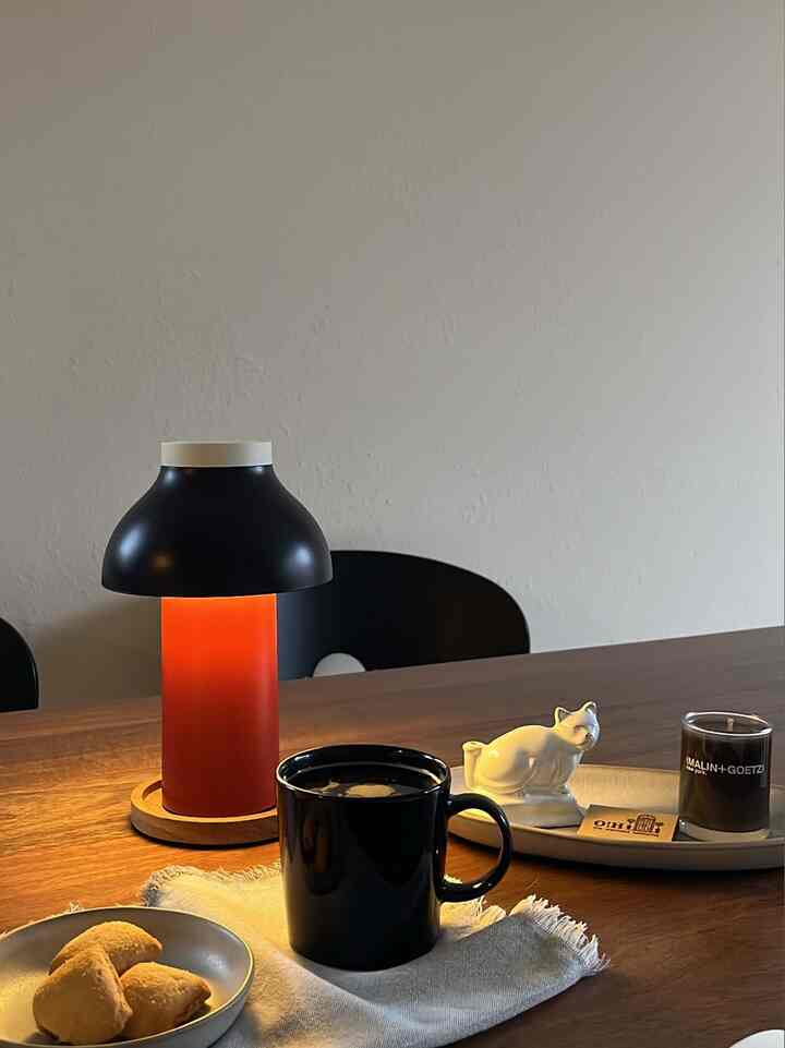 Warm wood tone dining table with black mug, table lamp, and candle creating a cozy home cafe atmosphere