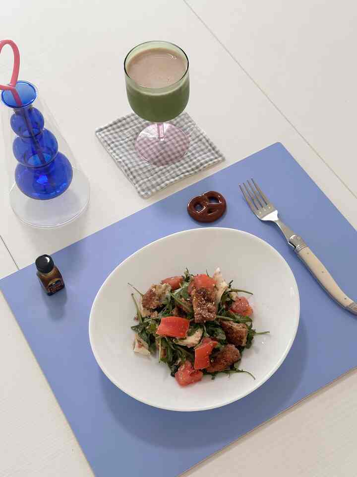 A simple home cafe setup on a white dining table featuring a blue placemat, salad plate, and wine glass with a pink stem