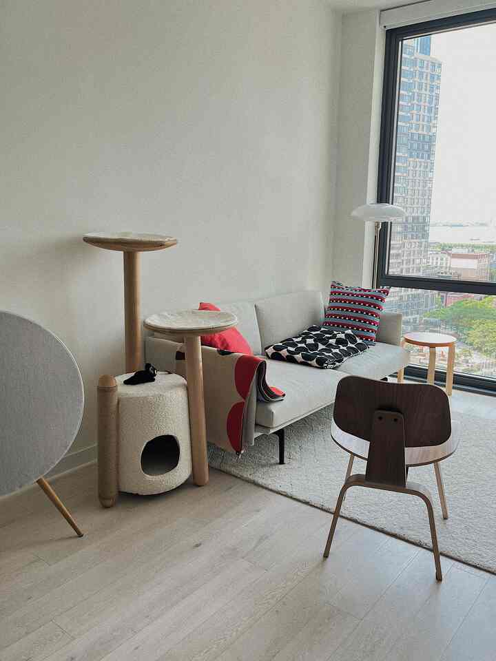 White and wood-tone living room featuring modern sofa and cat tower, creating a simple and natural space