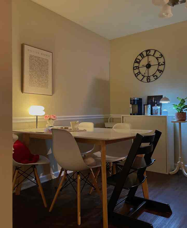 Beige and brown toned dining room featuring white dining table, chairs, clock and lamps in a cozy setting