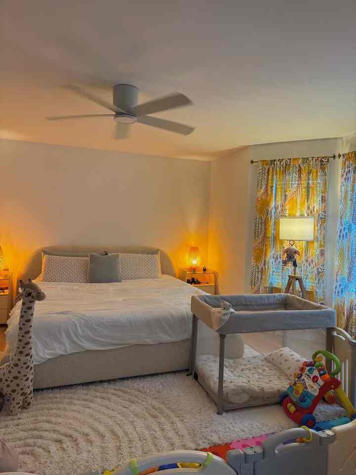 A warm and cozy beige and white bedroom featuring a baby playpen and various toys, creating a comfortable family space