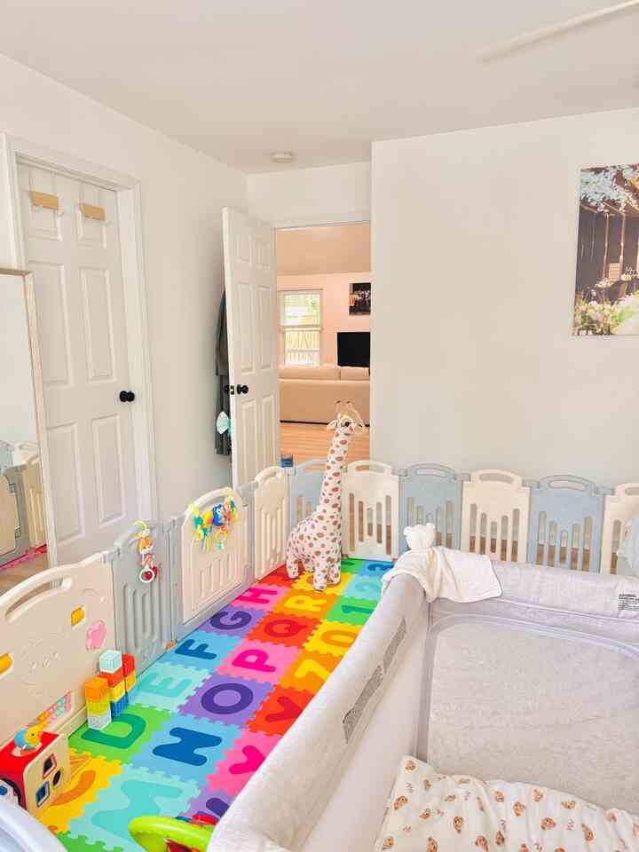 Bright white and beige kid's room featuring an alphabet floor mat and baby safety fence creating a cozy play area