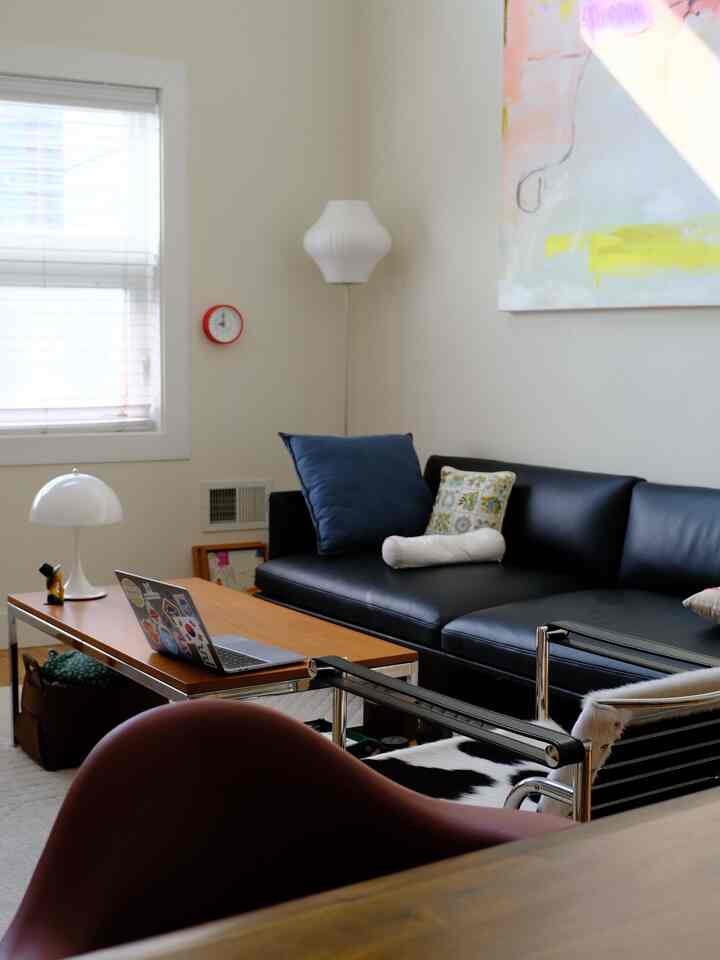 Modern living room with white walls, black leather sofa, navy cushions, and minimalist furniture