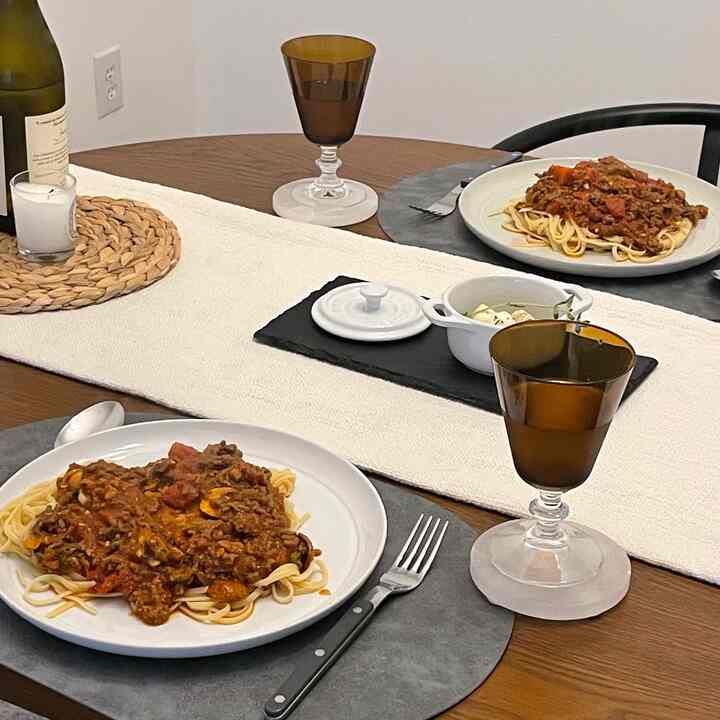 Brown wooden dining table with white table runner in a two-person dining room featuring pasta plates and wine glasses creating a cozy atmosphere.