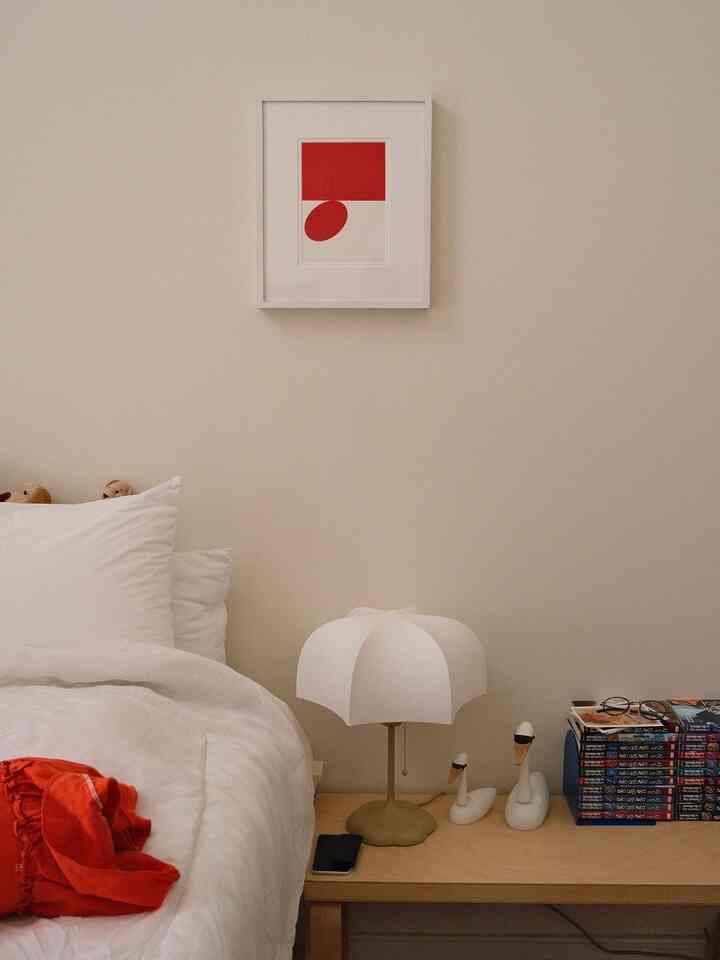 White and beige toned bedroom corner featuring unique table lamp, wooden bench, and abstract wall art in cozy atmosphere