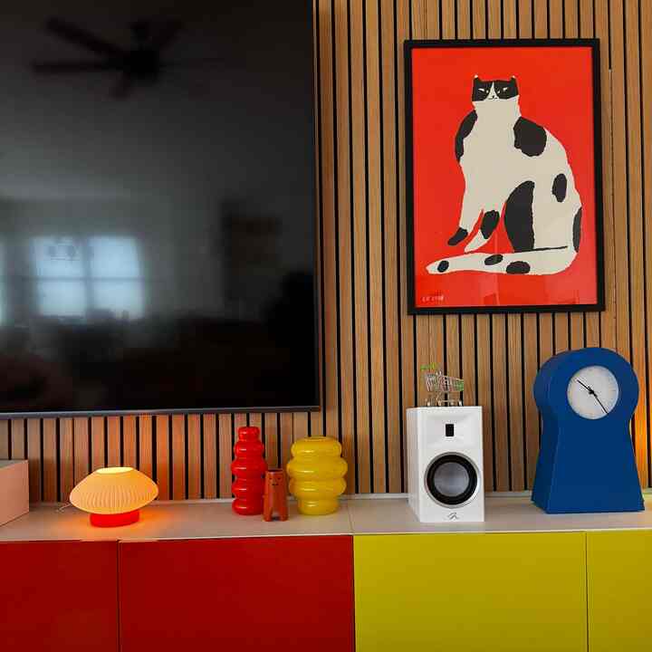 Modern living room with wood slat wall, colorful red, yellow, and blue furniture, and cat artwork decor