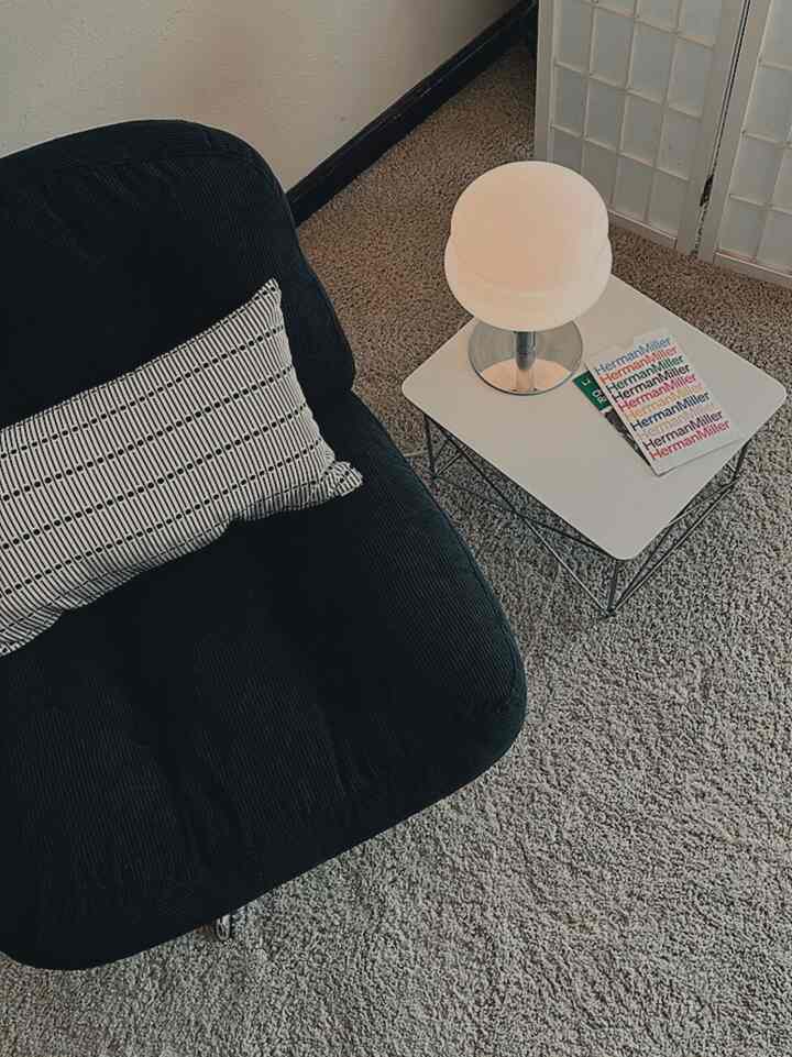 Beige-toned compact living room featuring a black armchair, small white coffee table, and table lamp in a modern setting