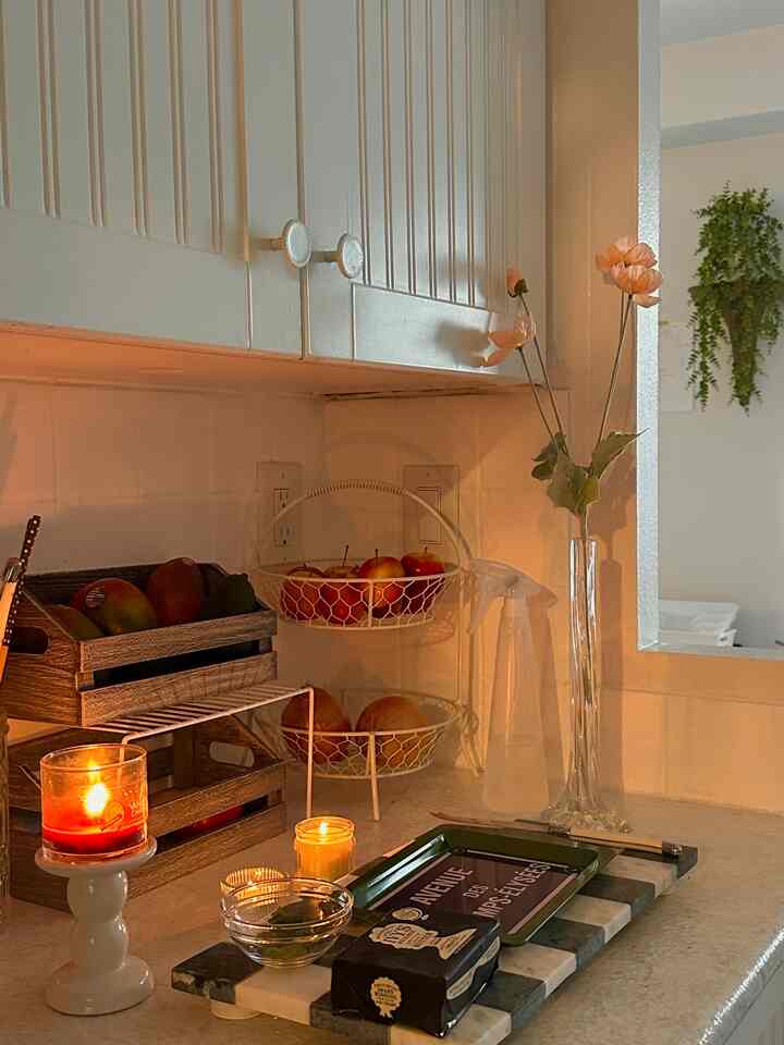 Warmly lit white-toned kitchen featuring candles, tableware, and plants creating a cozy atmosphere
