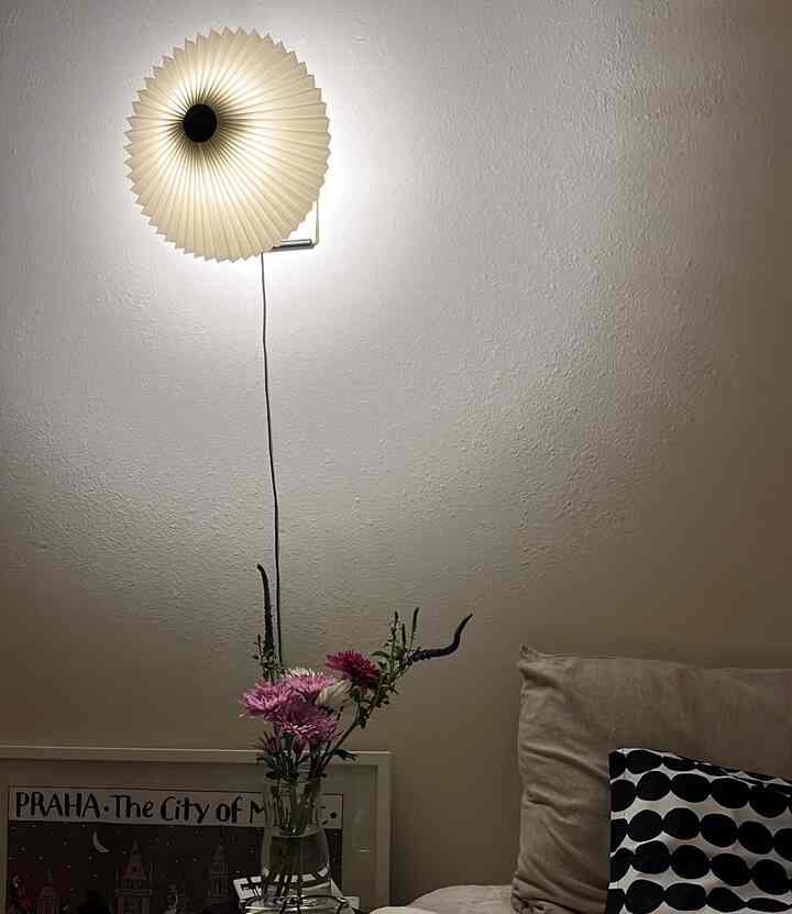 Cozy bedroom space with warm white wall and wall sconce, beige sofa with vase of flowers and black patterned cushion