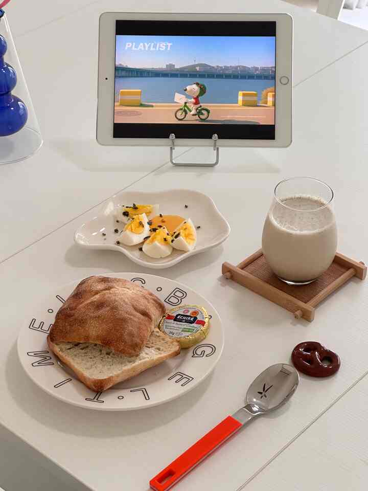 White-toned kitchen dining table featuring bread, boiled eggs, a beverage, and an iPad on a simple clean surface