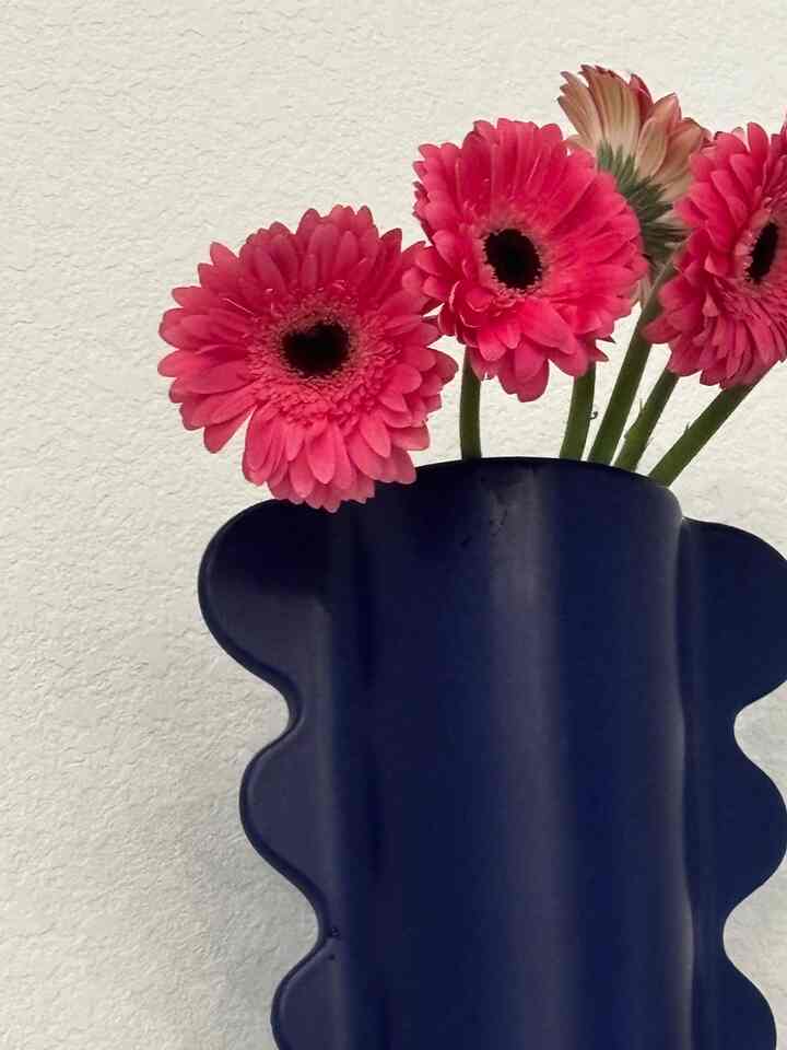 Navy vase holding vibrant red gerbera flowers against a textured white wall, showcasing stylish decorative elements