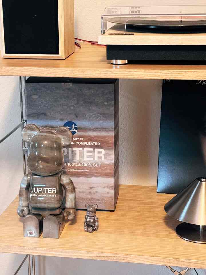 A modern bedroom corner featuring natural wood tone shelves with a record player and Bearbrick collectible objets
