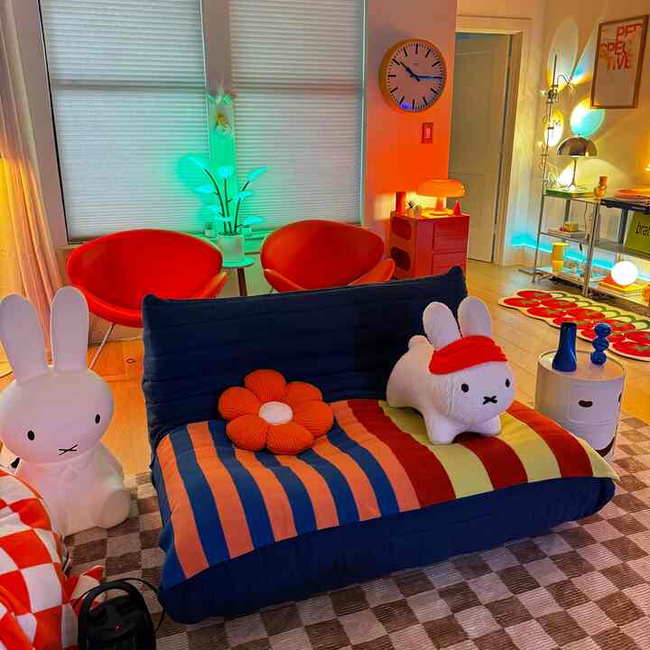 A vibrant red and blue toned living room featuring two red chairs and a blue sofa adorned with a flower cushion and a rabbit plush, creating a cozy atmosphere