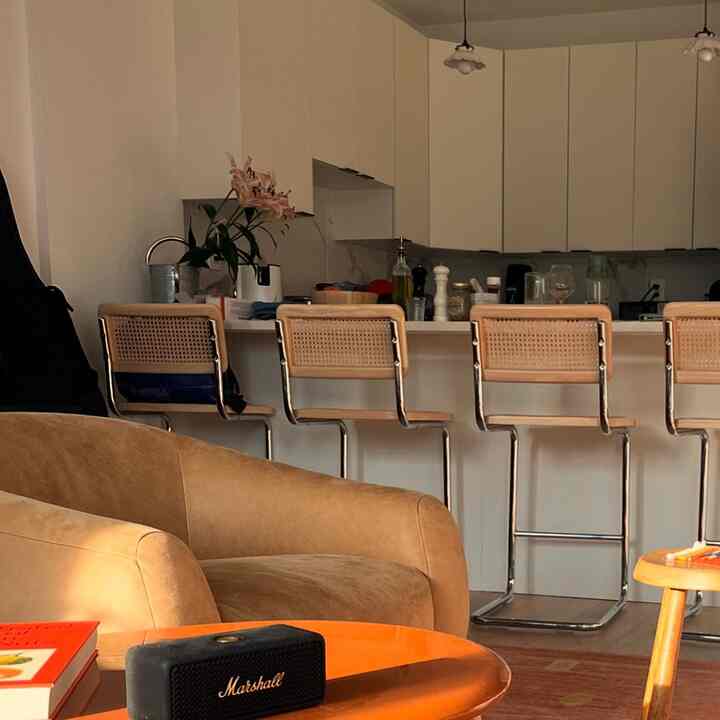 Warm brown leather armchair and bar stools placed in white kitchen and living room space with a cozy modern vibe