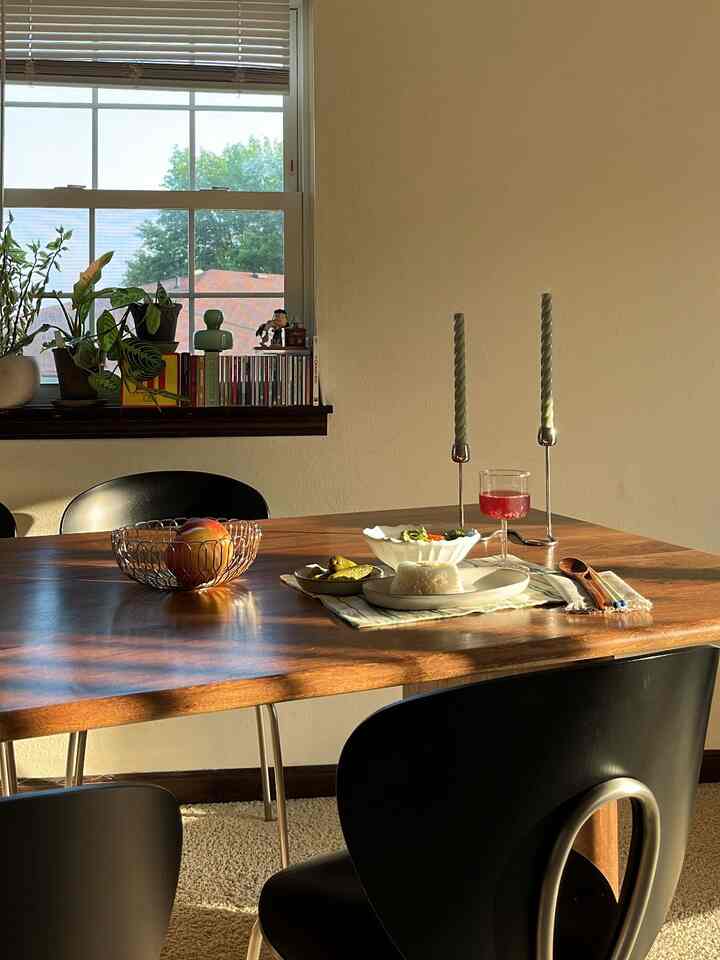 Warm wood tone dining room with black dining chairs, natural light streaming through window creating cozy atmosphere