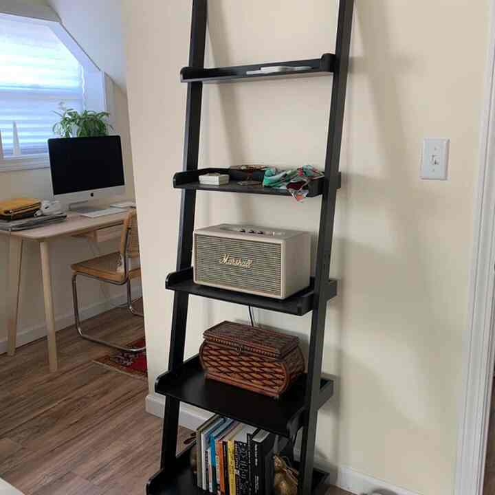 Natural-toned living space featuring a black ladder-style shelf and wooden desk, presenting a neat and functional home office vibe