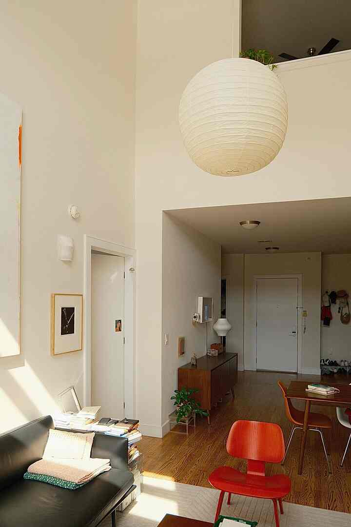 Natural modern living room featuring wood flooring, white walls, black sofa, red Eames lounge chair, and a large pendant light with abundant natural light