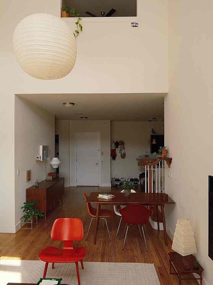 A beige-toned dining room with wood-toned flooring, featuring a red armchair and wooden dining chairs, showcasing modern style