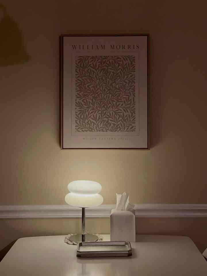 Beige-walled dining room with white dining table, featuring a glowing table lamp and wall decor in a minimalist setting