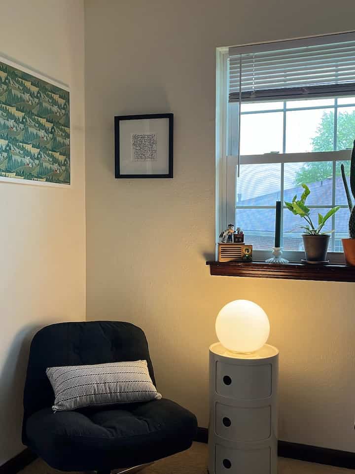 A cozy living room corner with white walls and a window, featuring a black armchair and spherical table lamp