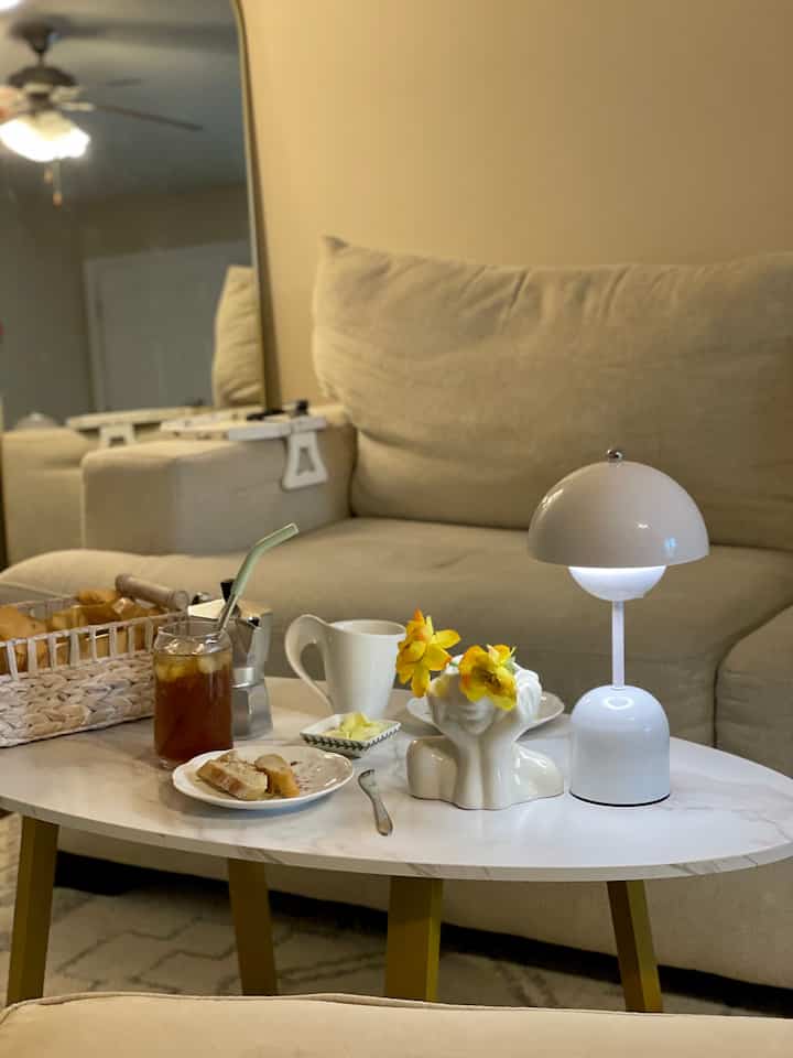 Beige-toned living room featuring a sofa, white coffee table with vase and table lamp in a cozy setting