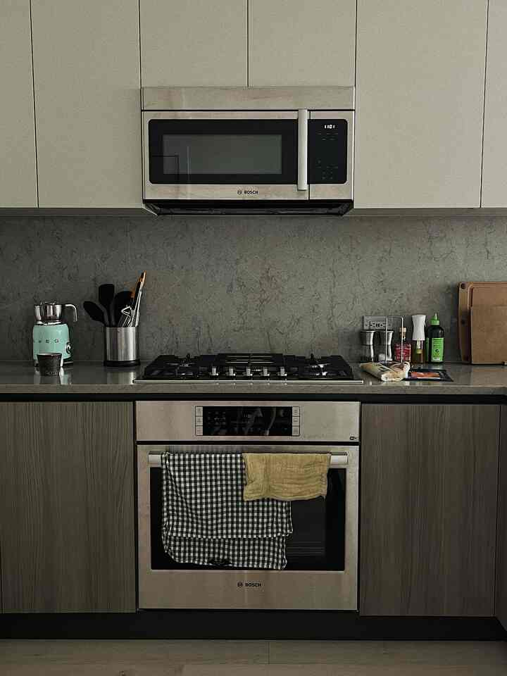 Modern kitchen featuring gray marble backsplash, wood tone lower cabinets, and stainless steel appliances
