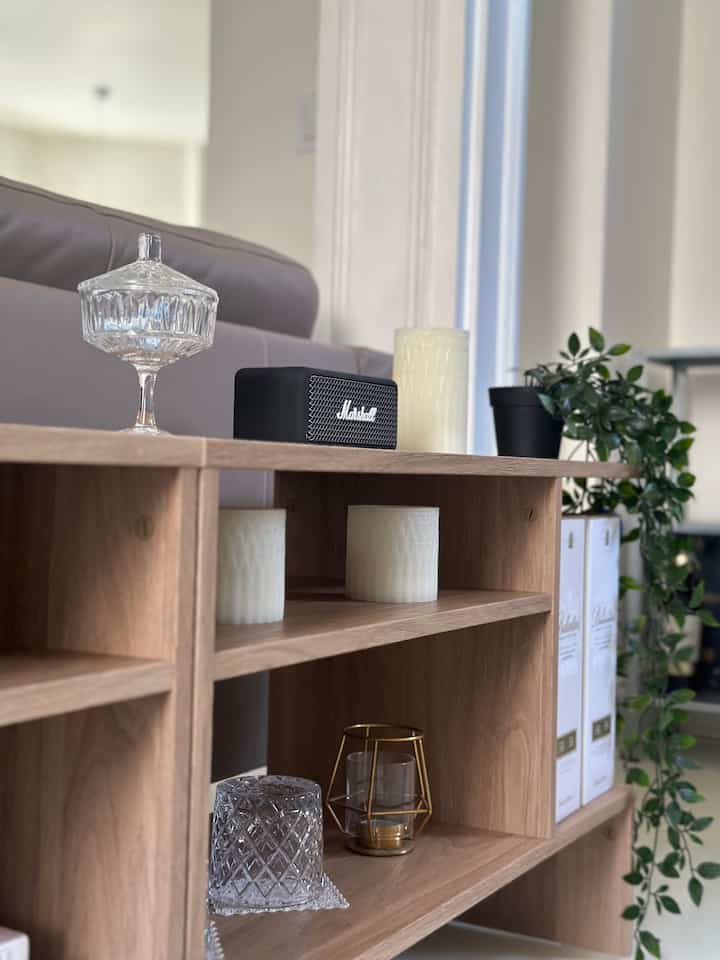 Natural wood tone side table with gray sofa in a simple living room, featuring a green plant and black audio device as accents