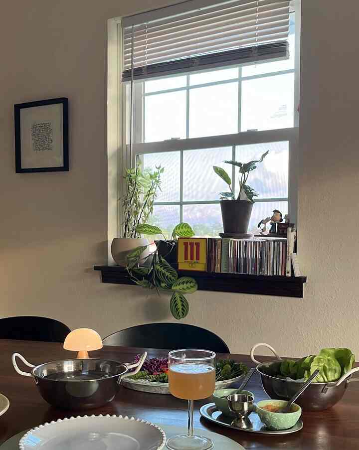 Cozy kitchen dining area with warm natural light, plants on the window sill, and table set with dishware and wine glass