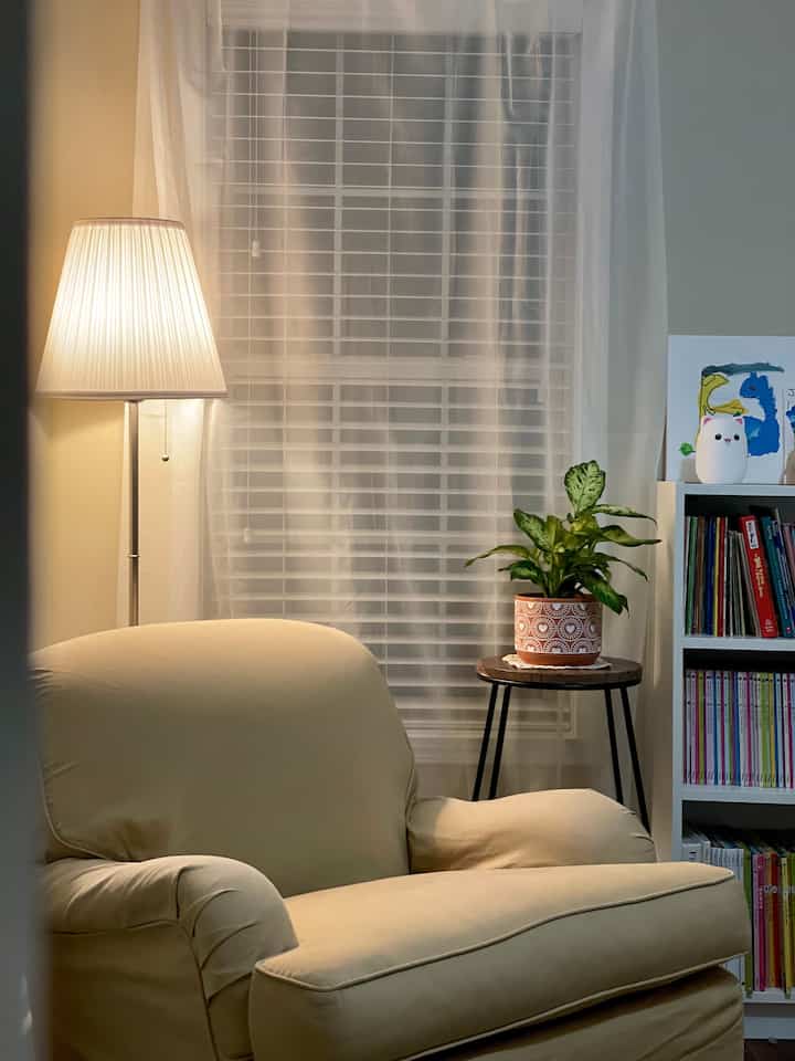 Warm beige and white toned kids' room featuring a cozy armchair, floor lamp, and bookshelf for a comfortable reading nook