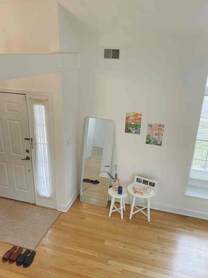 A white and wood tone entrance featuring a large mirror and small stools, creating a clean and cozy interior space