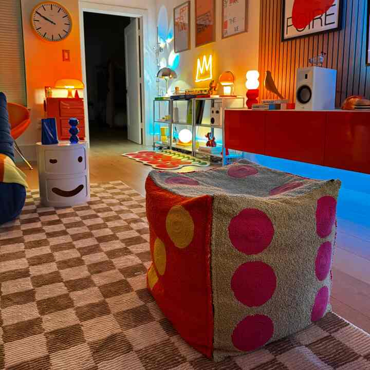 Modern living room with bold red and yellow accents, featuring colorful lighting and a patterned dice pouf stool