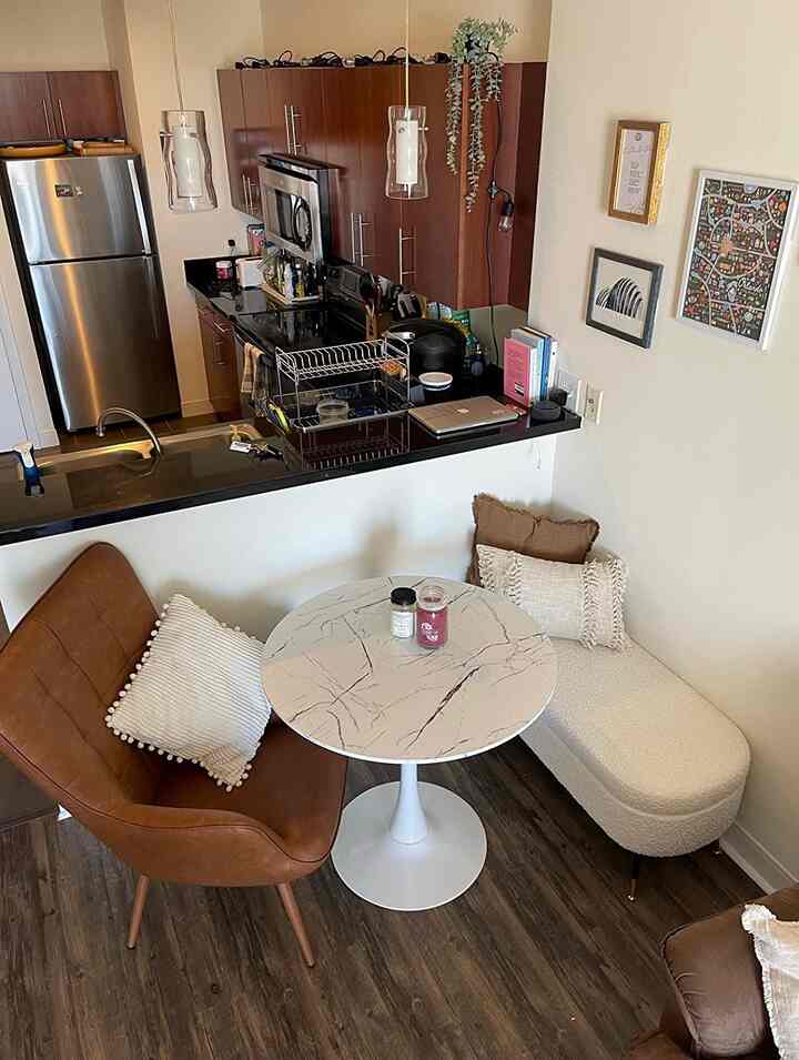 Brown and white toned kitchen dining room featuring a round marble dining table, leather armchair, and cozy cushions creating a warm atmosphere