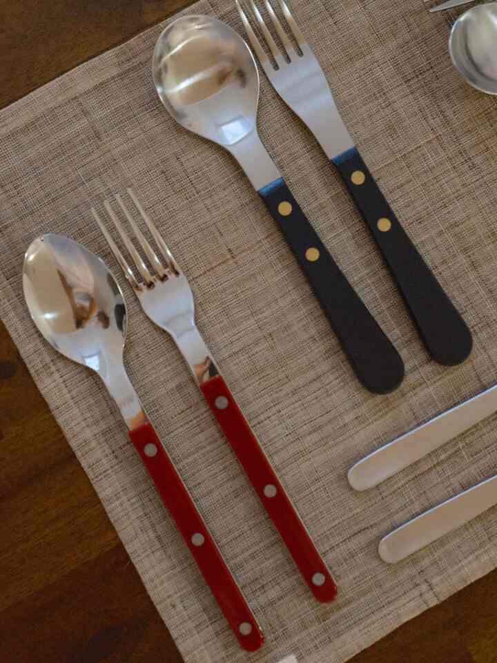Cutlery set with red and black handles placed on a beige woven tablecloth