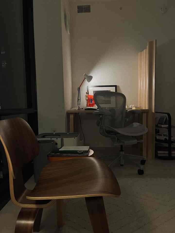 White-walled home office with wood tone furniture, featuring a single workspace chair and desk lamp creating a cozy atmosphere