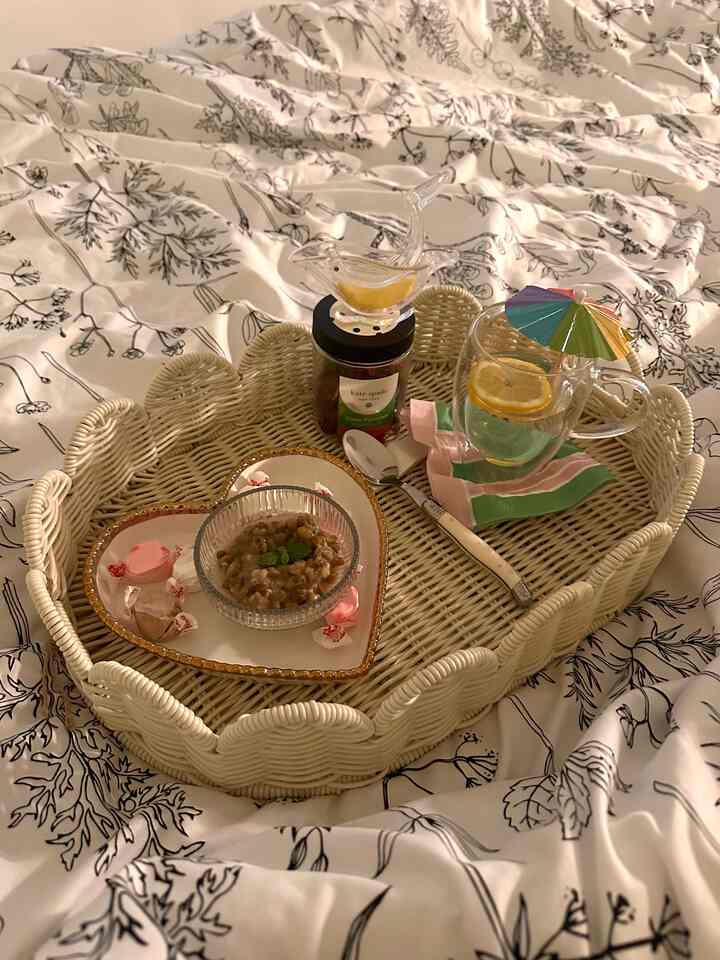 Cozy and romantic home cafe setup featuring a wicker tray with dessert and drink on white-black floral patterned bedding