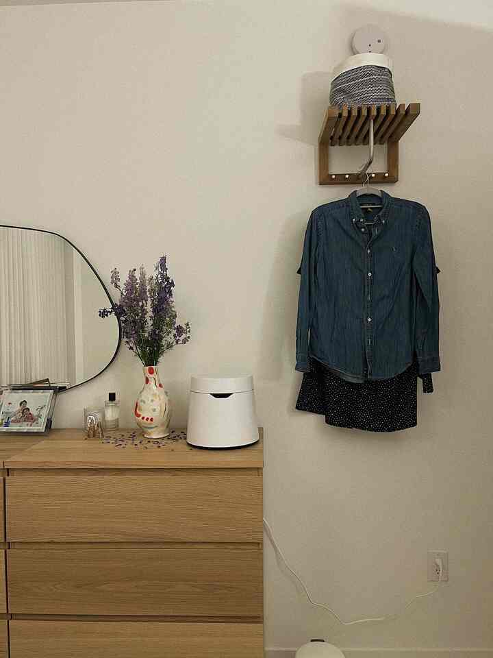 A natural space with white and wood tones, featuring a dresser and wall shelf neatly arranged with a vase and clothes