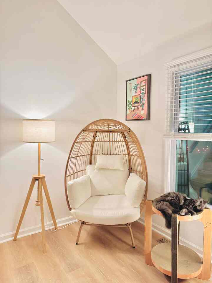 Natural wood-tone living room corner with white walls, a floor lamp, cozy armchair, and a cat resting on a pet bed