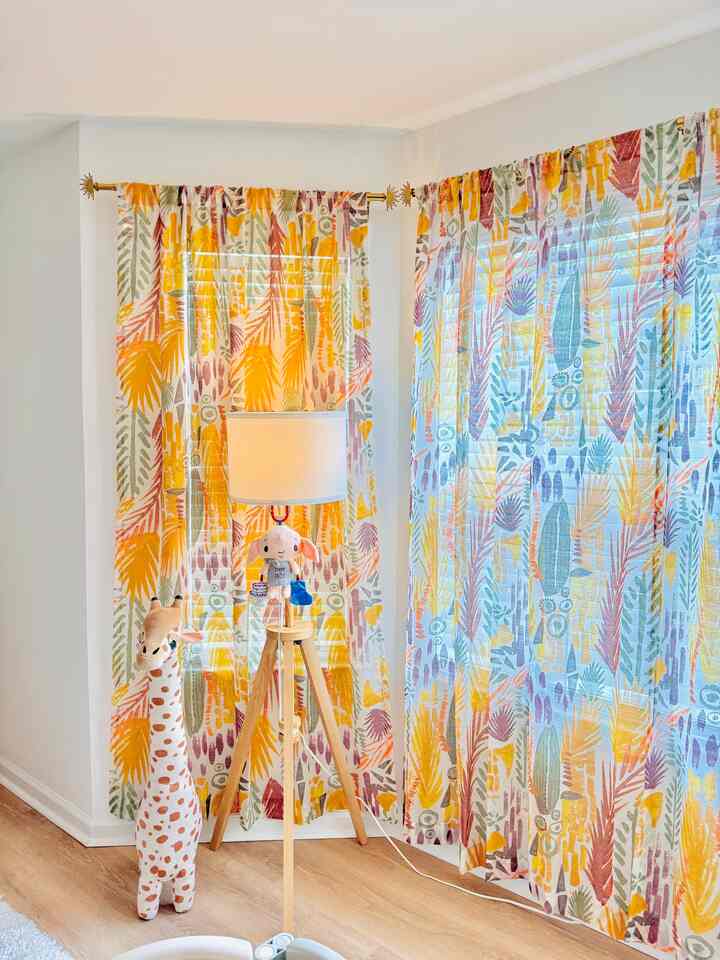 Bright light brown floor and white walls with colorful patterned curtains, wooden floor lamp, and children's toys in a cozy kids' space