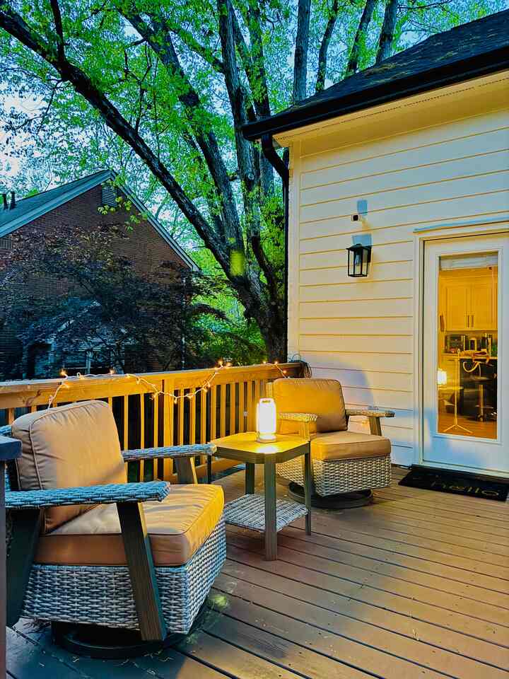 Brown wood-tone balcony featuring two cushioned outdoor chairs, a small table, and string lights creating a cozy outdoor setting