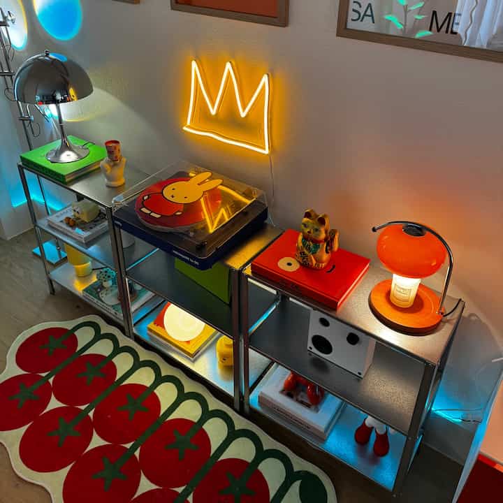 Cozy retro industrial living space with yellow neon light and Miffy turntable on metal shelves above a vibrant tomato runner rug