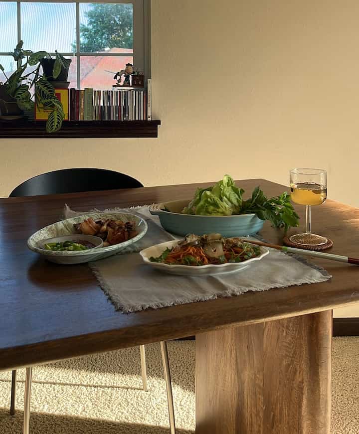 Natural wood tone dining table in a simple dining room with white walls, featuring oval plates and tableware
