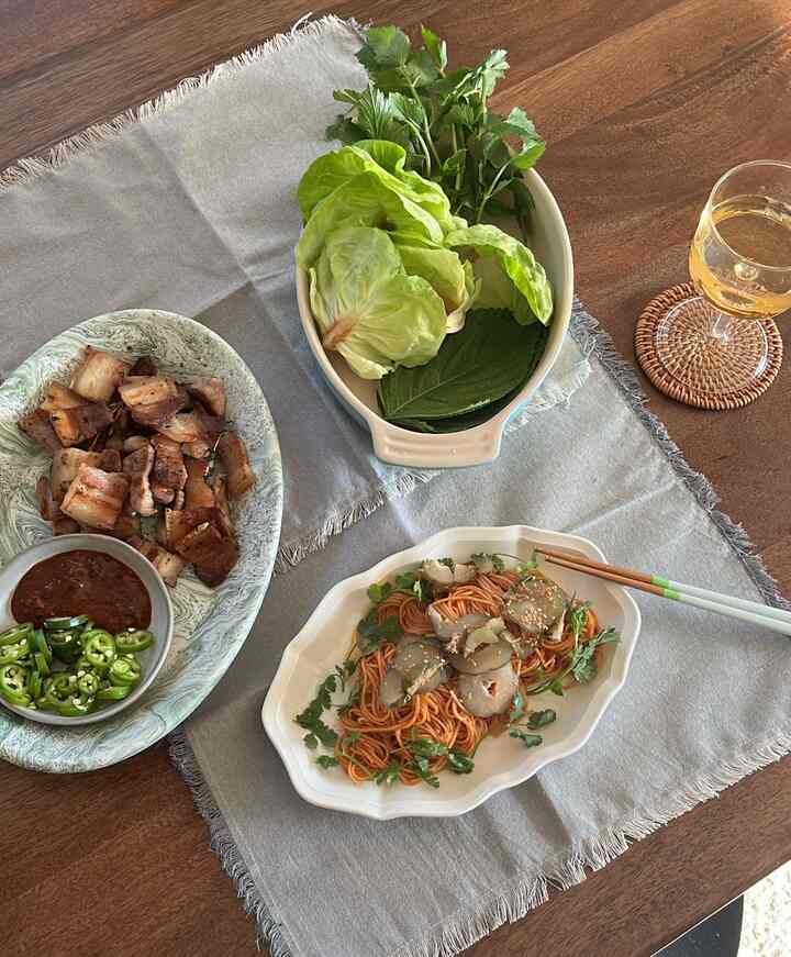A natural color dining room featuring a wooden dining table with gray table runner, oval dish, bowl, cutlery, and wine glass in a clean dining setup